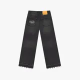 Pantalón de jean negro con corte baggy, de tiro medio y pierna ancha. Presenta un parche de cuero naranja en la cintura trasera y un bolsillo trasero con un parche bordado de la marca Nude Project. El ruedo tiene un acabado deshilachado.
