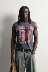 Musculosa gris oscuro de ajuste relaxed, con cuello redondo y diseño sin mangas con sisa amplia. En el frente presenta una estampa estilo varsity en tonos bordó y blanco con la inscripción "Local Team 94 One Step Daily".