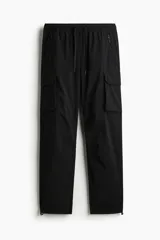 Pantalón cargo negro de nylon, corte recto y holgado, con cintura elástica y cordón ajustable. Presenta bolsillos cargo grandes en las piernas, bolsillos laterales y traseros con cierre, y cordón ajustable en los bajos.
