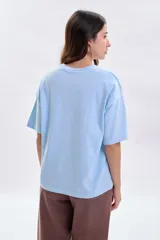 Remera de corte boxy color celeste, con mangas cortas y cuello redondo. Presenta la palabra 'Buongiorno' bordada en el frente en color marrón.