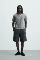Bermuda de corte relajado, color gris oscuro con efecto tie-dye o textura irregular. Presenta cintura elástica ajustable con cordón y bolsillos laterales y traseros de plastrón.