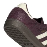 Championes Adidas Samba OG de color bordó con textura símil piel de serpiente y detalles en blanco marfil. Cuentan con las clásicas tres tiras laterales, inscripción 'SAMBA' en letras doradas, refuerzo de gamuza en la puntera y suela de goma marrón.
