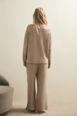 Sweater de punto de textura suave y diseño holgado, con cuello redondo y mangas largas. Presenta un tono beige melange y un corte ligeramente más corto en la parte frontal.