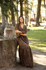 Vestido largo de lino con escote en V, mangas largas abullonadas y falda con volado en el ruedo. Presenta un estampado floral en tonos tierra sobre base marrón.