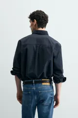 Camisa de corte regular fit confeccionada en tejido de algodón. Presenta cuello con solapa abotonada, cierre frontal con botones, manga larga con puños abotonados y un bolsillo plastrón en el pecho.