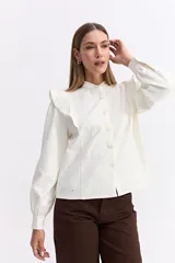 Camisa de color bordó con cuello mao y cierre frontal de botones. Presenta volados en los hombros que aportan volumen y un diseño sofisticado.