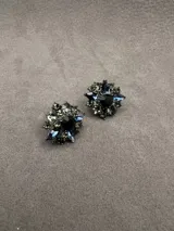 Aros de diseño floral con cristales en tonos azul, gris y negro, con un cristal central oscuro y base metálica.