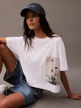 Remera blanca de algodón con corte cropped y mangas cortas. Presenta un estampado fotográfico floral de Calvin Klein en el lateral.