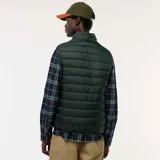 Chaleco tipo puffer de color verde oscuro, con cierre frontal completo, cuello alto y diseño acolchado horizontal.