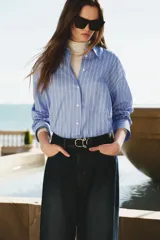 Camisa oversize de popelina a rayas celestes y blancas, con cuello clásico, mangas largas, bolsillos en el pecho y cierre frontal de botones.