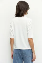 Remera negra de cuello redondo y manga tres cuartos, confeccionada en tela con textura sutil. Presenta fruncidos laterales que aportan caída y movimiento a la prenda.