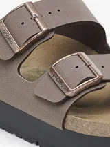 Sandalia tipo slide de dos tiras ajustables, color marrón topo, con hebillas metálicas color oro rosa. Presenta una plataforma gruesa de color negro sobre la clásica suela de corcho anatómica de Birkenstock.