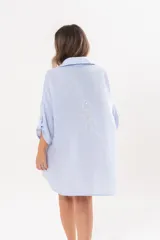 Vestido camisero de lino color celeste, con escote en V, cuello clásico, cierre frontal de botones y mangas tres cuartos regulables. Diseño holgado con corte asimétrico.