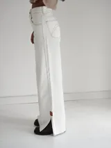 Pantalón vaquero de tiro alto y corte recto, color blanco, con aberturas laterales en los bajos y detalles de terminación en cuero.