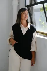 Chaleco de punto negro con escote en V profundo y diseño de trenzas verticales en el frente. Presenta un corte holgado y terminaciones en tejido acanalado.