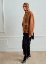 Abrigo corto de paño en color camel, con cuello alto, cierre frontal de botones y bolsillos laterales con solapa. Presenta un diseño de corte recto y estructura holgada.