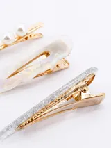 Set de tres pinzas para el pelo: una dorada con perlas, una transparente con detalles iridiscentes y una plateada con glitter.