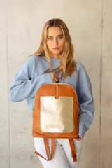 Mochila de cuero color tostado con bolsillo frontal dorado y cierre plateado.