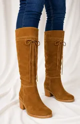 Bota de caña alta color suela, confeccionada en cuero napa, con diseño de caña caída y ajuste mediante cordones en la parte superior. Presenta un taco cuadrado foliado de 4,5 cm y suela de goma antideslizante.