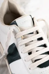 Zapatillas urbanas de cuero blanco con una franja lateral verde oscuro y suela color crema.