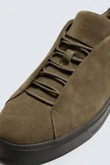 Zapatilla de estilo urbano confeccionada en piel con acabado de serraje. Presenta un diseño minimalista con cordonera oculta y suela de goma a contraste.