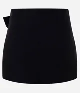 Short pollera mini de tiro bajo, confeccionado en bengalina negra. Presenta un diseño de cintura cruzada con detalle de hebilla ovalada metálica en el frente.