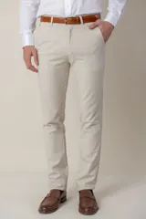 Pantalón de vestir color beige, de corte clásico, con bolsillos laterales y traseros. Se ajusta a la cintura con cinturón de cuero marrón.