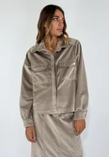 Chaqueta color beige de terciopelo con cuello camisero, cierre frontal con botones, dos bolsillos de parche en el pecho y manga larga.