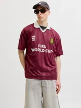 Camiseta de estilo deportivo con cuello polo en color blanco y cuerpo en color bordó con diseño de rayas verticales sutiles. Presenta estampados frontales con la inscripción 'FIFA WORLD CUP' y 'CAN MEX USA', junto con un parche conmemorativo de la FIFA.