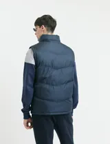 Chaleco capitoneado de color azul marino con cierre frontal completo y cuello alto. Presenta un diseño acolchado con costuras horizontales y forro interior con estampado escocés.