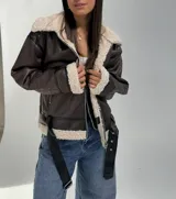 Campera tipo aviador de cuero sintético color chocolate con interior y cuello de corderito sintético color crema. Presenta cierre frontal, bolsillos laterales con cierre y cinturón ajustable en el ruedo.