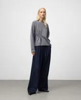 Jersey de punto color gris, con cuello redondo y manga raglán. Presenta un detalle de frunce central ajustado con un broche metálico plateado.