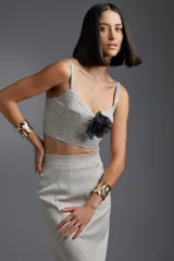 Top blanco con estampado de lunares negros, breteles finos y detalle de flor negra en el centro del busto.