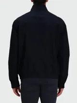 Chaqueta tipo bomber o Harrington de color azul oscuro, con cuello alto abotonado, cierre frontal de cremallera y pequeño logo bordado en el pecho.