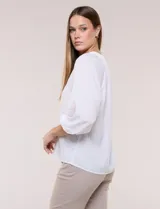 Blusa de gasa de color lila con calce holgado, cuello a la base con escote en V y cartera de botones a tono. Cuenta con fruncidos en el cuello y hombros que otorgan volumen, manga tres cuartos estilo abullonado con puño elastizado y ruedo suavemente redondeado.