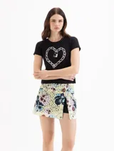 Minifalda de encaje estampado con diseño floral en tonos amarillos, celestes y marrones, que integra un short de poplín negro por debajo. Presenta un tajo frontal y detalles de volados de cuero.