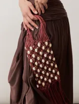Cartera tipo bolso de mano confeccionada mediante técnica de tejido de red en cordón marrón, decorada con cuentas de madera y detalles de flecos en la parte inferior.