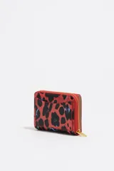 Billetera pequeña de estructura rígida con acabado brillante y estampado animal print en tonos rojos y negros. Presenta cierre de cremallera perimetral, logo metálico dorado en el frente y tarjetero interior.