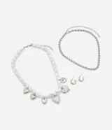 Conjunto de bijouterie de metal plateado, compuesto por dos collares y un par de aros. Incluye una cadena de esferas, un collar de cuentas orgánicas blancas estilo perla con dijes colgantes de corazones y aros, y aros pequeños tipo argolla con cierre de perno.