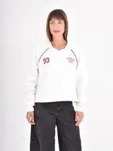 Buzo azul oscuro de corte holgado con cuello polo y escote en V. Presenta mangas largas con costuras raglán en color blanco y un estampado frontal con la palabra Ambience y el texto United Nation League en tonos dorados.