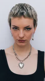 Collar de cadena plateada con dije de corazón con pinchos, detalles de espada y pin de gancho con pinchos.