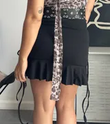 Minifalda negra con volado inferior y ajustable a los lados. Material elastizado y opaco.