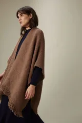 Ruana tejida en punto texturizado color marrón chocolate, con terminación de flecos en los bordes. Diseño inspirado en la vestimenta tradicional uruguaya, confeccionada en una mezcla de fibras suaves y ligeras.