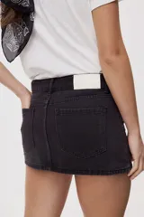 Falda mini de denim azul con calce al cuerpo y tiro medio. Presenta bolsillos delanteros amplios, doble botón en la cintura y aplicaciones de tachas metálicas que recorren la cintura y los bolsillos.