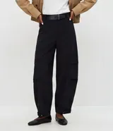 Pantalón barrel de viscosa color negro, de corte ancho con diseño redondeado en las piernas y bajo ajustado. Presenta pinzas laterales, trabillas y un cinturón fijo de PU con hebilla metálica.