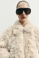 Chaqueta tipo bomber de textura afelpada en color crema, con cuello solapa, cierre frontal con cremallera y puños y cintura de tejido elástico acanalado.