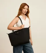 Cartera grande Satinato de color negro, confeccionada en poliéster con detalles en poliuretano. Cuenta con compartimento principal con cierre de cremallera, solapa frontal con broche a presión y doble asa de hombro.