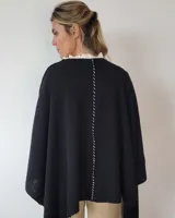 Ruana de lana color negro, beige y tostado, con diseño geométrico y flecos en el borde inferior.