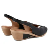 Sandalia de cuero negra con puntera abierta y talón cubierto. Cuenta con una tira trasera con hebilla y una plataforma de goma color beige con tecnología Care Juanetes.