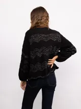 Campera de punto con cierre frontal bidireccional, mangas largas abullonadas y diseño calado con patrón de ondas en color negro con detalles brillantes.